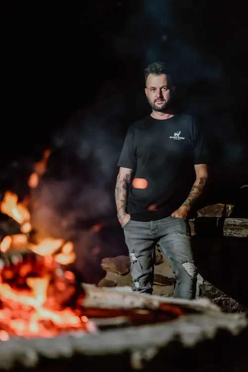 Chef Wayne standing beside an open fire at night