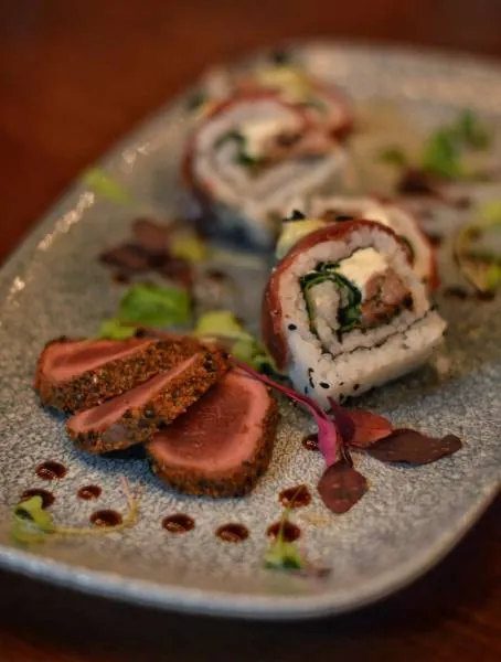 Seared springbok sashimi and California rolls on a stone plate